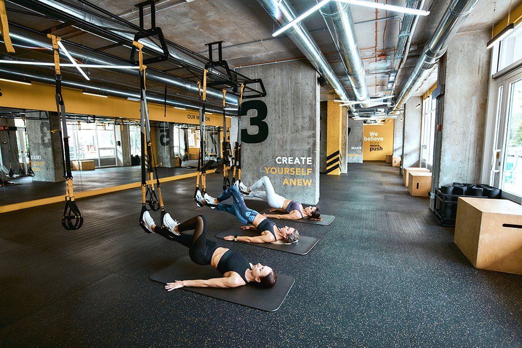 Strength training. Three young caucasian athletic women in sportswear exercising with fitness trx straps at industrial or gym