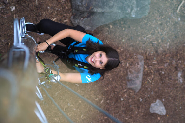 nainen kiipeää hymyillen ylöspäin seikkailupuistossa