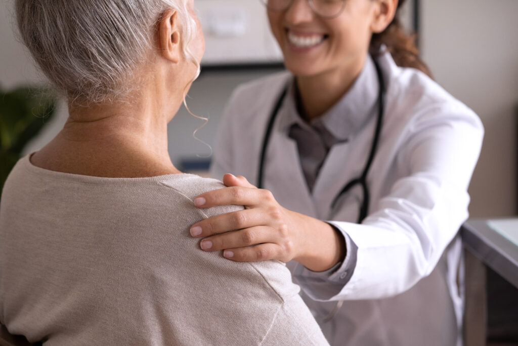 Close up back view smiling female doctor wearing uniform touching mature patient shoulder