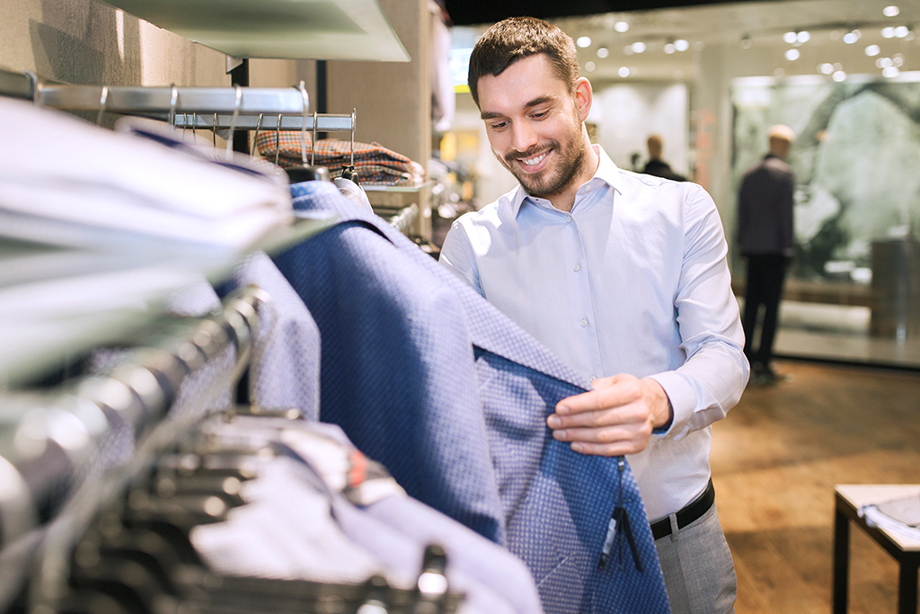 happy young man in shirt choosing jacket in a clothing store